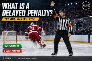 NHL referee raising an arm to signal a delayed penalty as the fouled team pulls its goalie for a sixth attacker